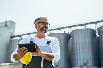 worker using tablet in front of grain silo