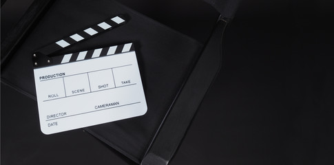 White Clapper board or movie slate and black director chair use in video production or movie film and cinema industry on black background.