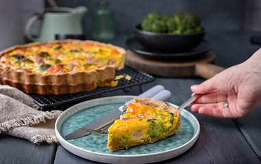 Traditional broccoli pie with salmon and cheese. Food from healthy and healthy foods. Lunch. Tarte is divided into portions and hands in the frame. Dark photo.