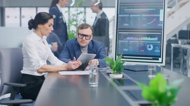 In the Meeting Room Female Executive Shows Digital Tablet Computer to Creative Venture Capitalist, They Discuss Statistics and Investment Capital. Busy Corporate Office with Businesspeople Working