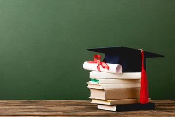 books, academic cap and diploma on wooden surface isolated on green