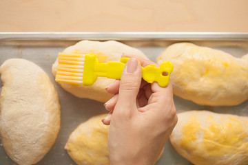 Homemade uncooked patties from yeast dough with stuffing are lying on a naing tray, hand with brush lubricateы them by raw egg and ready for baking.