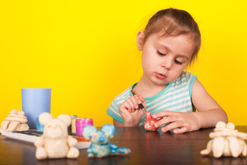 Little girl paints toy animals paints on a yellow background