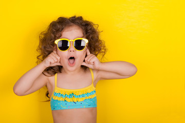 Little girl in a bathing suit and sunglasses on a yellow background