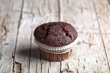 Fresh single dark chocolate muffin on rustic wooden table.