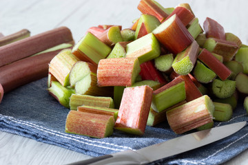 Pile of sliced rhubarb and knife on a blue tea towel with a grey wood background