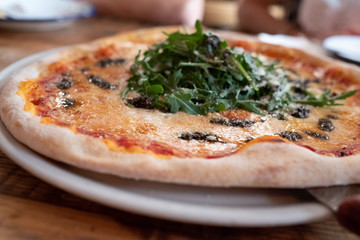 Stone pizza with provolone cheese, tartufata and arugula on wooden table