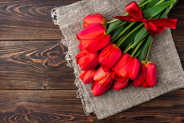 Red tulips with red ribbon on dark wooden background.