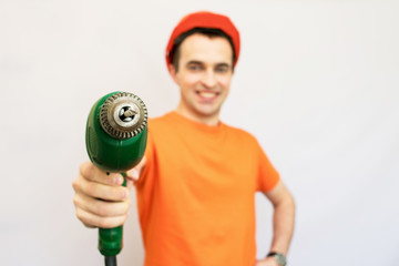 Handsome construction worker with protective helmet on his, directs the camera hand electric drill, looking into the camera, isolated