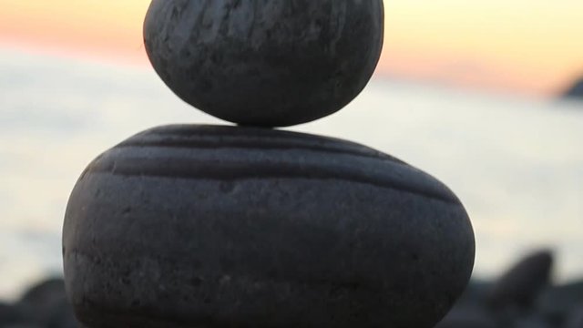 Fun holiday at the sea, beach activities. The pyramid (cone) is built of round stones (small boulders) in balance (equilibrium), against the sunset