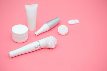 Face and body skin care. Devices for cleansing the skin, trimmer from unwanted hair. Set of cosmetic white tubes and jars on a pink coral background. Spa home care treatments. 