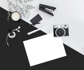 Black and grey color background with flower branches, a cup of milk, earphone, pen, stapler, camera, name card and white paper. Architect and designer background with copy space.