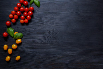 Tasty cherry tomatoes and basil leaves on black rustic table.  Top view with copy space. 