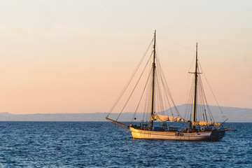 Fototapeta premium Yacht in the Mediterranean Sea at sunset, luxury travel tour, space for text, summer, ocean surface, water transport, fishing, vacation, two-masted yacht,