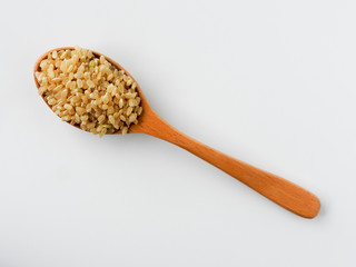 Top view of raw brown rice (also called hulled rice, unpolished rice,husked rice) on wooden spoon isolated on white background. Rich nutrition. Asian food,Health, agriculture concept. With copy space.