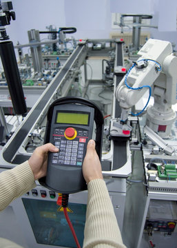 Man is pushing button on teach panel to control a robotic arm which is integrated on smart factory production line. industry 4.0 automation line which is equipped with sensors and robotic arm.