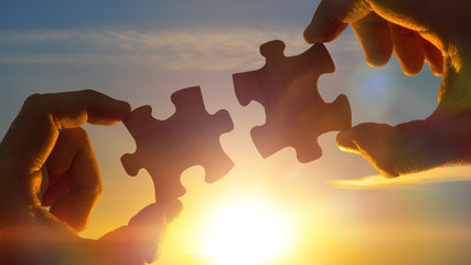 two hands connect the puzzle details, against the sky of the sun. Business concept idea, partner,...