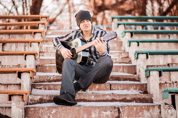 Obraz premium Young man sitting on steps playing guitar and singing, music concept
