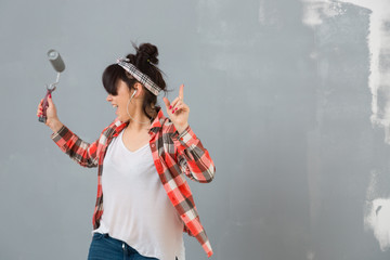 Woman dancing and singing while painting a wall in her apartment. DIY home renovation.