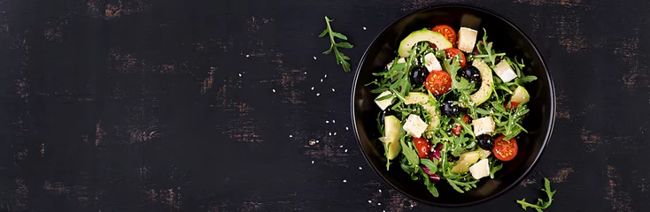 Fotobehang Green salad with sliced avocado, cherry tomatoes, black olives and cheese. Healthy diet vegetarian summer vegetable salad. Table setting. Food concept. Banner. Top view. © timolina