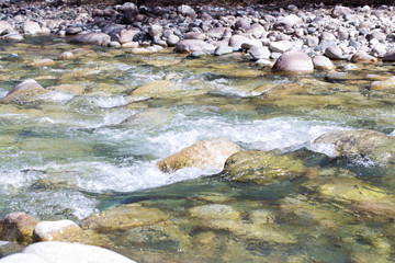 Water in the mountain raging river. Beautiful natural background of stones and water. Texture of clear water and fast river. Backdrop with copy space