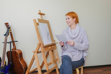 Young attractive woman draws behind an easel.