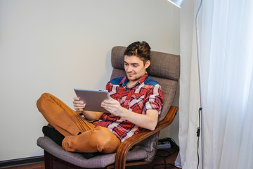 A man uses a digital tablet sitting in a chair.