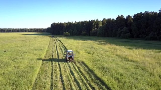 close flight above haymaker mower driving on boundless field cutting off hay grass against pictorial landscape