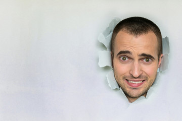 Afraid man making hole in paper, looking at the camera, the awkward moment, shocked, blue...