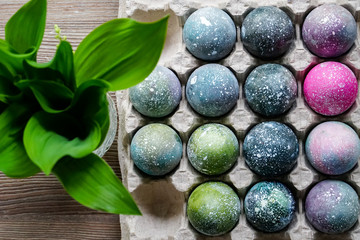 Boiled Easter eggs painted in the style of cosmos and a distant galaxy, against the backdrop of an antique tree and a beautiful flower. Easter.