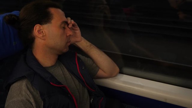 Man get some sleep wile travelling at regional train, portrait of passenger leaning to window with eyes closed. Late evening international journey