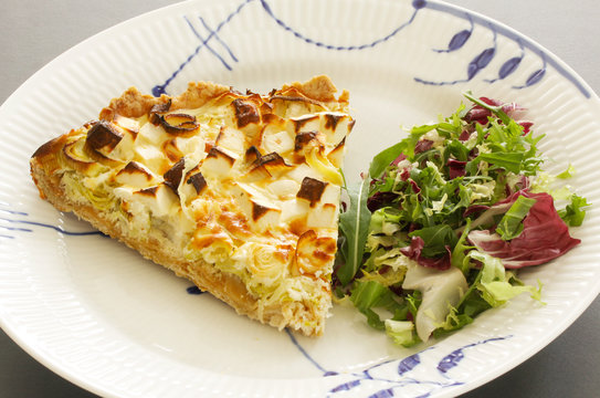 A slice of quiche with leek and feta or goats cheese on a plate with crispy leaf green salad. Vegetarian food image close up.