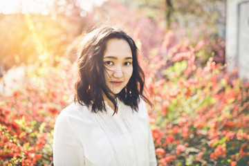Cheerful asian young woman in a white blouse in a blooming park.