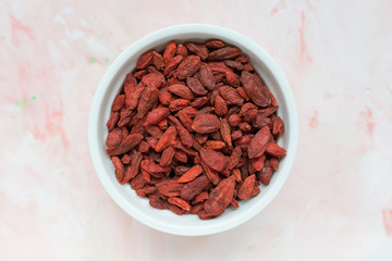 Dried goji berries in a porcelain bowl on a pink background