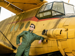 A handsome young pilot standing next to an old plane