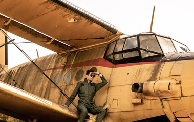 A handsome young pilot sitting on the wing of a plane and covering the sun