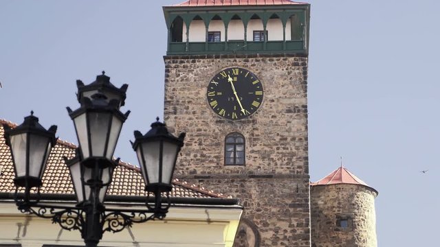 Medieval Renaissance square with stone tower and clock. View to row of houses with colorful old facades and blue sky. Age-old gas lamp and arcades. Static sunny day shot, color corrected footage