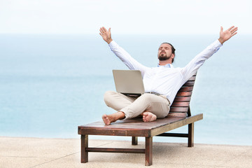Young businessman on the beach resting on his deck chair using his tablet - Powered by Adobe