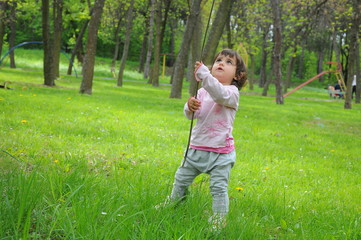 A little girl is playing with stick in the grass in the park