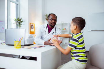 Dark-skinned doctor giving bowl with sweet candies to his lovely son
