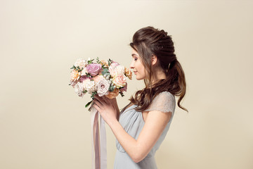 Elegant girl with a haircut in a soft blue dress and make-up is holding a bouquet of a stylish bouquet of flowers.