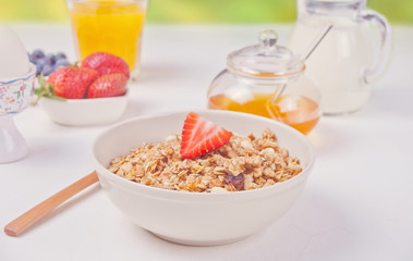 Muesli with strawberries, honey, milk on the white table on nature on background