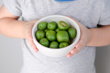 Mini kiwi in a plate in the hands of a child. Small exotic fruits on white background.