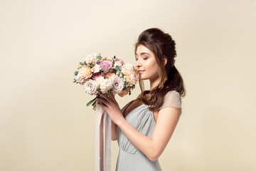 Elegant girl with a haircut in a soft blue dress and make-up is holding a bouquet of a stylish bouquet of flowers.