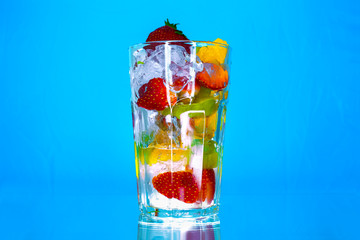 Dessert layered in a transparent glass, mineral water, orange, kiwi, nuts on a bright blue background background. The concept of healthy, proper and simple Healthy food
