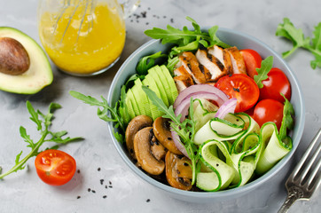 Healthy salad bowl with chicken, mushrooms, tomatoes, cucumbers, avocado and arugula
