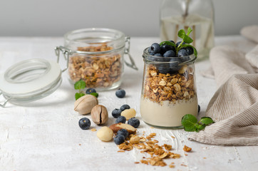 Healthy breakfast - glass jars of granola with fresh blueberries, yogurt, nuts and mint. Granola on a light background, space for text.