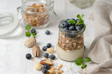 Healthy breakfast - glass jars of granola with fresh blueberries, yogurt, nuts and mint. Granola on a light background, space for text.