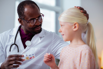 Dark-skinned doctor touching head of cute blonde girl