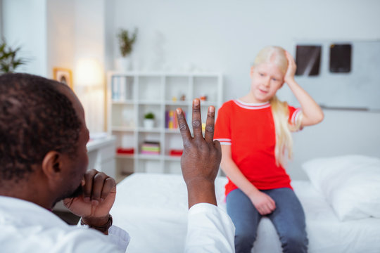 Dark-skinned doctor showing girl with concussion three fingers
